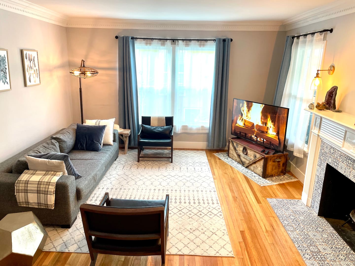 The cozy living room at Amie's Leimert Park home, with a grey sofa, leather armchairs and a tiled fireplace